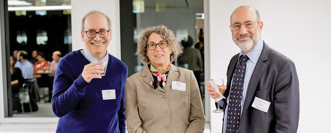 Two men and a woman in a room; the windows behind them reflect other conference attendees